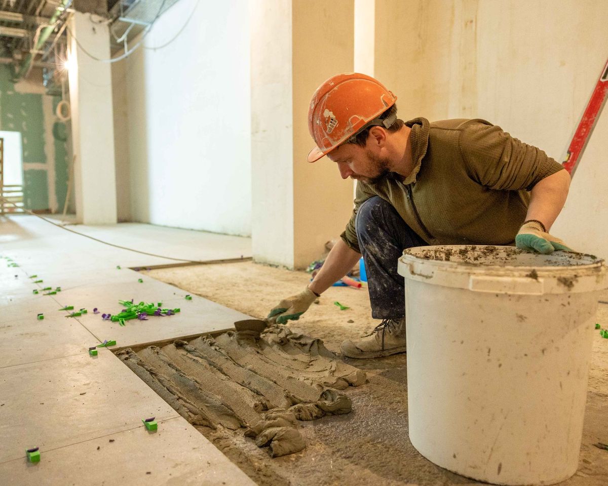 Tegelzetter strijkt tegellijm uit op een vloer in renovatie